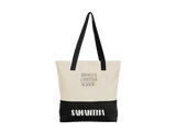 A personalized cotton twill tote bag with a cream upper section, black bottom panel, and black shoulder straps. The front features a 5"x3.125" ADVOCATE CHRISTIAN ACADEMY logo in gold and black lettering, with the name "Samantha" in white all caps in the black bottom panel.