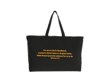 A black canvas tote bag with gold printed text from Ephesians 2:10 on the front, set against a plain white background.